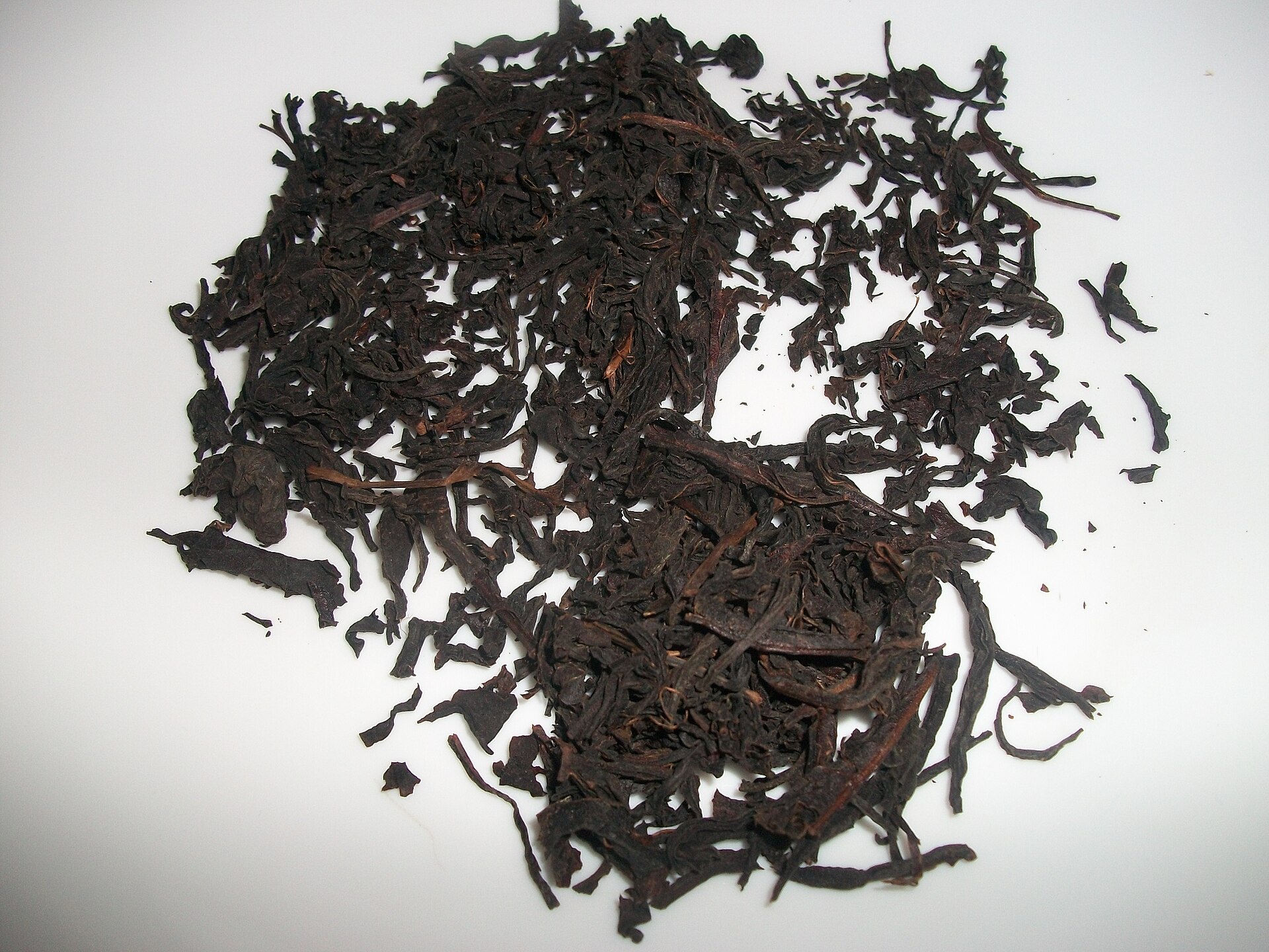 A strong cup of black tea beside its spent leaves