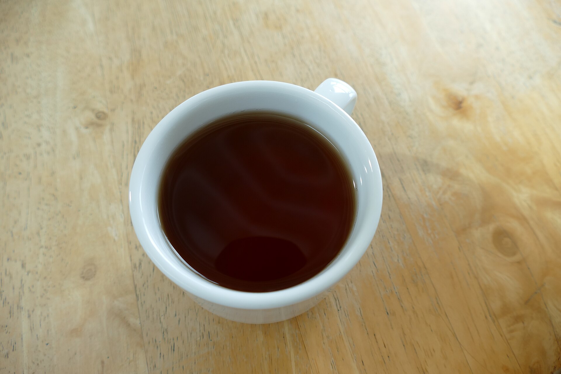 A cup of black tea on a saucer with tea leaves nearby